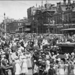 Image: a huge crowd of men, women and children in early 20th century dress gather in a city street in celebration. Written on the photograph are the words "King William St, Adelaide: 12.11.18"