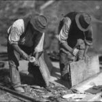 Image: Two men in hats are bent over splitting slate