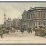 Image: horse drawn buses and carts travel down a busy city street lined with large commercial buildings