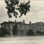 Image: Two large, multi-storey historic buildings, one of which has columns bordering its front door