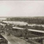 Image: a collection of stable buildings on the bank of a river.