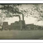 Image: A factory with two large chimneys spews black smoke.