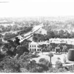 Image: A man stands on the roof of a large, two-storey building bounded by a road and a wooded area