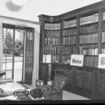 Image: A room containing shelves full of books and a wooden desk with chair