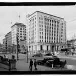 Image: An nine storey art deco concrete "sky scraper" on the corner of two city streets. The building features bronze windows and is faced with cream coloured stone on the upper floors and polished granite at street level