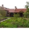 Image: A single storey bluestone cottage with red brick quoins and a red tin roof.