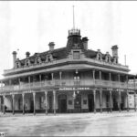 Image: A large corner building with balcony, mansard roof, and flagpole