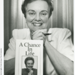 black and white image of a woman sitting at a desk with a book