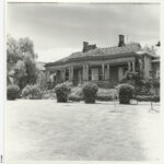 Image: Black and white photograph of the Anlaby house front lawn. House features mullioned windows, and deep set veranda supported by doric columns