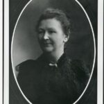 Image: A closeup portrait of a woman wearing a black dress with her hair tied back