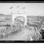 Image: Crowds of people watching cars drive through arch