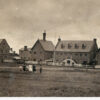 Image: six children, four girls and two boys, walk across a grass paddock in front of a complex of two storey stone buildings with steeply pitched roofs