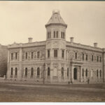 Image: A large, two-storey stone building in Victorian Italianate style. One corner of the building features an octagonal tower with an additional storey