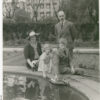 Image: A balding, moustachioed, middle-aged Caucasian man in a 1940s-era suit poses for a photograph with his wife and two young children. One child is a boy, and the other is a girl