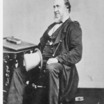 Image: Black and white photograph of older man on a chair, circa 1860