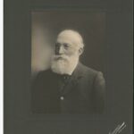 Image: A photographic portrait of an elderly man with a full, white beard and wire-rimmed glasses