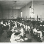 Image: A busy telephone exchange. There are rows of switchboard operators and several other staff supervising