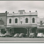 Image: 1950s era cars are parked on the street outside a two-storey terraced building with arched windows, a balcony and a stepped parapet with a sign reading Empire Theatre