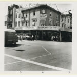 Image: a three storey corner shop with verandah. 1960s cars pass in front.