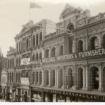 Image: a grand four storey department store with a highly decorative facade. The ground floor has plate glass windows with displays with the remainder of the floors having a large number of arched windows.