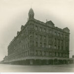 Image: a huge five storey hotel building on the corner of two wide dirt streets. The building has a rounded corner topped with a cupola.