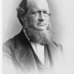 Image: Black and white photographic portrait of a man with small round glasses and a large beard