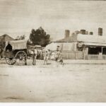 Image: horse and cart on dirt street with group of people, including young children, surrounding