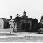 Image: a small stucco church with a belfry and small arched porch. Most of the windows have been filled in.