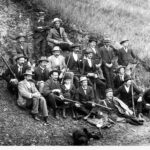 Image: Group of rifle club members sitting together on a hill holding rifles