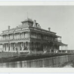 Image: large two story building with smaller third story and wrap around verandah