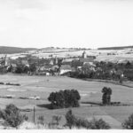 Image: A panoramic view of a German town. There are many houses. A number of large, open fields surround the town