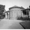 Image: A single storey bluestone building with rounded wall, arched portico and verandah