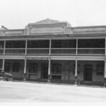 Image: A two storey hotel built into a terrace with 1920s era cars parked outside