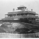 Image: large two story building with smaller third story and wrap around verandah