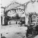 image: black and white shot of man driving his cargo-laden horse under a botanically-decoratedarchway that reads, 'The Gardeners' and Market Salesmen's Association Welcome'