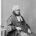 Image: Black and white portrait of a man, with the chin curtain beard popular at the time. He is seated and wearing his wig and gown.