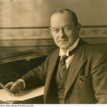 Image: portrait of a man in suit holding a card