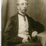 Image: Black and white portrait of a man with grey hair, mutton chops and a moustache. He is wearing a suit jacket, vest, shirt and tie.