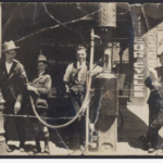 Two men and a boy with one of Adelaide's first petrol pumps, one with the hose in his mouth