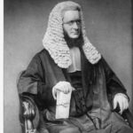 Image: Upper body portrait of a man, seated, wearing his wig and gown and holding a sheaf of papers.