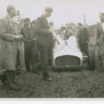 Image: A group of young Caucasian men in late 1940s attire stand next to three period racing cars