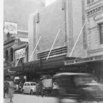 Image: 1930s era cars speed past the art deco facade of the new Woolworths building