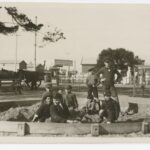 Image: A group of children play in a sandbox in a park. A street and buildings are visible in the background