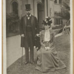 Image: Man in suit and top hat next to women sitting in dress and hat