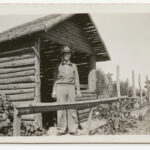 Image: man stands next to building made of logs