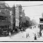 Image: a busy city street lined with three and four storey ornate stone buildings