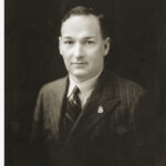 Image: Black and white portrait photograph of the upper body of a man dressed in formal attire