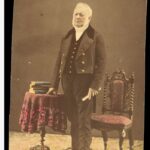 Image: coloured image of man standing next to chair and books