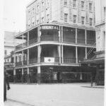 Image: A five storey corner building with balconies on the second and third floors.