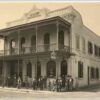 Image: a group of men, a woman and a boy in 1870s attire stand outside a two storey hotel with a balcony, arched windows, and a parapet sign which reads "A.KLAUER WHITE HEART HOTEL"